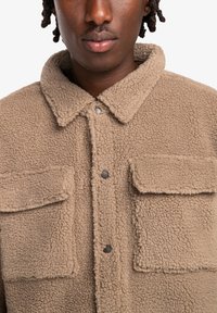 Beige fleece jacket featuring a collar, two front pockets, and snap buttons. Overall textured surface with soft, thick material.