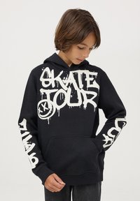Felpa nera con cappuccio, caratterizzata da testo bianco in stile graffiti "SKATE TOUR" sulla parte anteriore e sulle maniche, con tasca a marsupio classica e cappuccio regolabile con cordino.