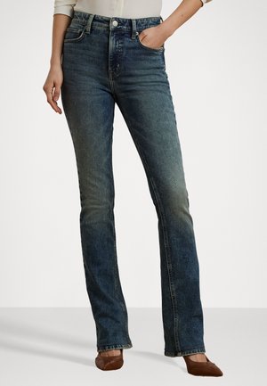 Blaue Denim-Jeans mit leichtem Schlag, ausgestattet mit Fronttaschen, Steppnähten und einer ausgewaschenen Optik. Kombiniert mit braunen Schuhen.