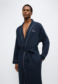 Ναυτικό μπουρνούζι με μακριά μανίκια, κατασκευασμένο από μαλακό βαμβάκι. Διαθέτει αντίθετη λευκή πιπίλα και κεντημένο λογότυπο στο στήθος.