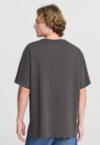 T-shirt grigia in cotone con una vestibilità rilassata, maniche corte e collo rotondo. Design semplice senza motivi o grafiche, che mette in risalto uno stile sobrio.