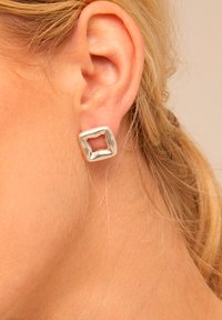 Pendientes de plata de ley con forma cuadrada, con un centro hueco y bordes texturizados. Vista de cerca que resalta el diseño y el material.