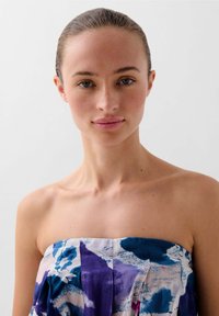 Strapless dress with a multi-colored pattern in purple, blue, and white. Smooth fabric texture with pleats along the bodice.