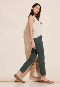 Ljusgrå ärmlös topp, gröna tapered byxor, bruna slip-on skor, bärandes en vävd väska. En enkel, avslappnad outfit med en ledig passform.