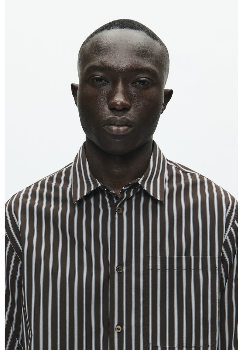 Chemise à boutons rayée marron avec des rayures verticales bleu clair et blanches, dotée d'une poche poitrine et d'un col classique.