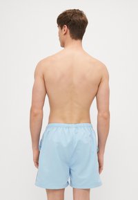 Bañador azul claro hecho de tejido suave con una cinturilla elástica. Presenta bolsillos laterales y un ajuste relajado.