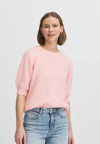 Lichtroze, geribbelde gebreide trui met een ronde halslijn en korte, opgerolde mouwen, gecombineerd met lichtblauwe jeans.