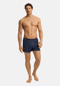 Modré plavkové šortky se vzorem a elastickým pasem, které ukazují geometrický design a lehkou tkaninu. Navrženo pro pohodlí.