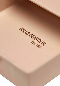 Interno di una scatola rettangolare rosa con il testo "Ciao Bella, Sì, Tu." stampato in marrone, caratterizzata da una superficie liscia e opaca.