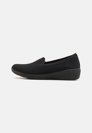 Sort slip-on sko med tekstureret strikket overdel og lav kile sål designet til komfort og afslappet brug.