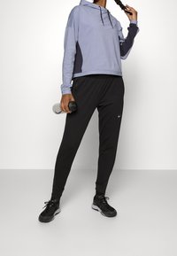 Lichtpaarse, gevoerde sporttop met donkere inzetstukken, gecombineerd met zwarte taps toelopende joggingsbroeken voorzien van een elastische tailleband en zijzakken.