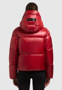 Chaqueta acolchada roja con un acabado brillante y una gran capucha. Presenta un parche de logo negro en la espalda, cremallera lateral y puños elásticos.