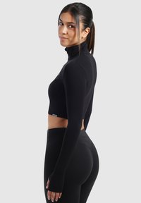 Schwarzes Crop-Top aus dehnbarem Material, mit langen Ärmeln, hohem Ausschnitt und Daumenöffnungen. Glatte Textur mit minimaler Markenkennzeichnung.