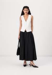 Colete branco sem mangas com um decote em V profundo e fecho de botão, combinado com uma saia preta de comprimento total. Inclui sapatos de salto preto com tira e uma bolsa.