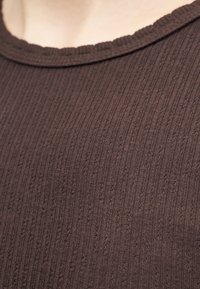 Κοντινό πλάνο καφέ ριγέ πλεκτού υφάσματος σε ένδυμα με στρογγυλή λαιμόκοψη σε φωτεινό δέρμα ως φόντο.