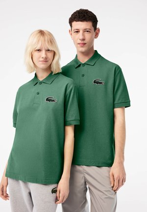 Polo verde in cotone, con colletto e tre bottoni, dotato di un logo ricamato sul lato sinistro del petto.