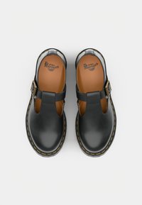Černé kožené Mary Jane boty s žlutým šitím, přezkami a světlým vložkami značky "Dr. Martens", z pohledu shora na bílém pozadí.