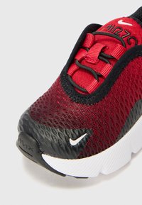 Baskets de sport rouges et noires avec tige en maille, col rembourré et semelle extérieure texturée. Présente le logo Nike et un système de laçage pour un ajustement sécurisé.