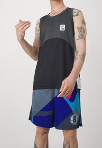 Czarny i szary top bez rękawów z logo, zestawiony z kolorowymi szortami z wzorem w odcieniach niebieskiego, szarego i czerwonego. Dopasowany krój, odzież sportowa.