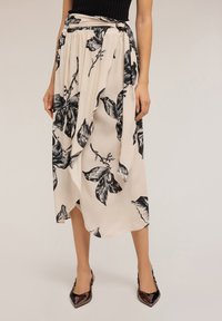 Gonna avvolgente beige con stampa floreale nera, vita arricciata con fibbia, indossata con un top nero e tacchi a punta lucidi su sfondo chiaro.