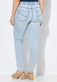 Svetle modré džíny s tapered střihem, elastickým pasem a dvěma zadními kapsami. V doprovodu hnědých, pletených mulek na podpatku.