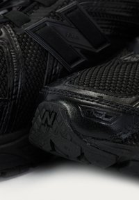 Black athletic shoes featuring a textured mesh upper, synthetic accents, and a patterned rubber sole with embossed logo for traction.