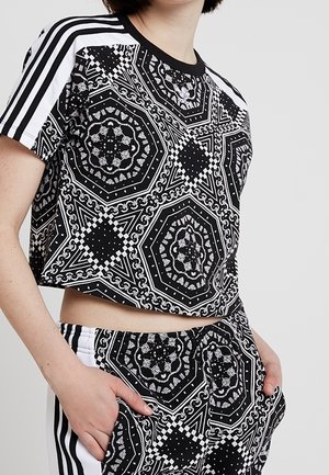 Camiseta recortada en blanco y negro con patrones geométricos. Presenta un cuello redondo, mangas cortas y rayas en contraste en los hombros.