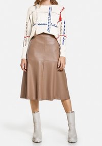 Creme sweater med farverig broderi og frynser, tilsat en brun plisseret faux læder nederdel og beige hælede støvler.