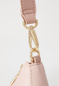 Sac à main en cuir rose avec une finition texturée, présentant un fermoir en métal doré et des accessoires en chaîne, mettant en valeur des détails de couture le long des bords.