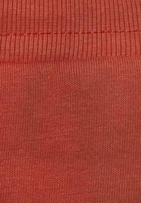 Tejido de ribete rojo que muestra una superficie texturizada con líneas finas y un patrón consistente, diseñado para la elasticidad y la comodidad.