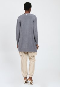 Grijze cardigan met lange mouwen en een afgeronde zoom, gecombineerd met beige joggers. Soepele textuur en ontspannen pasvorm met geribbelde manchetten.