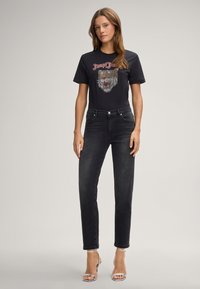 T-shirt noir graphique avec un design de lion, assorti à un jean droit sombre et des talons. Tissu lisse avec une silhouette ajustée.