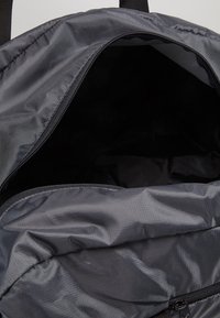 Avaa tummanharmaa reppu, joka näyttää tyhjältä sisältä ja osittain avatuilta pääosastolta, jossa näkyy vetoketju ja kankaan rakenne.