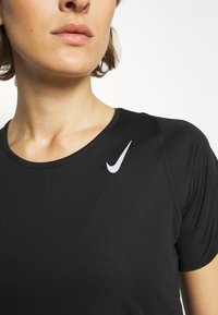 Schwarzes Sport-T-Shirt mit rundem Halsausschnitt und kurzen Ärmeln; verfügt über ein weißes Nike-Logo im linken Brustbereich; glatte Textur des Stoffes.