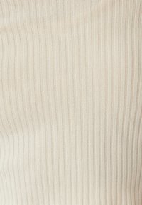 Tessuto a coste di colore crema con strisce verticali. La texture è morbida, con linee fini equidistanti. Materiale leggero e flessibile.