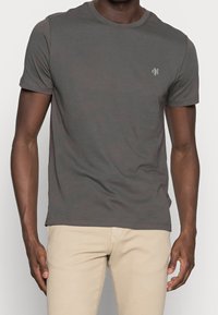 Šedé bavlněné tričko s kulatým výstřihem, krátkými rukávy a malým logem na hrudi. Měkká textura s klasickým střihem.