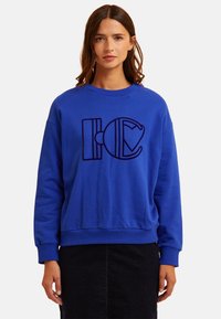 Blaues Baumwoll-Sweatshirt mit einem großen schwarzen Grafikdesign auf der Vorderseite, rundem Ausschnitt und gerippten Bündchen und Saum.