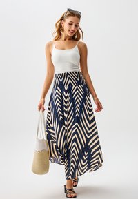 Falda larga azul marino con patrón de zigzag crema, cintura elástica, combinada con una camiseta sin mangas blanca y un bolso tejido beige.