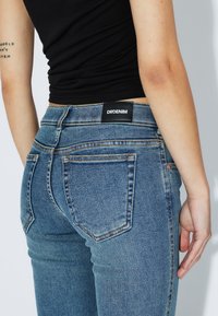 Blå denimjeans med hög midja och fem fickor. Sliten textur, kontrasterande sömmar och en svart DRDENIM-märke på baksidan.