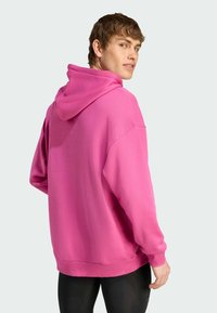 Lyserød hættetrøje med afslappet pasform, snoretræk i hætten og ribbede manchetter. Blød tekstur, enkel design, og går til hofterne. Sorte leggings bæres nedenunder.