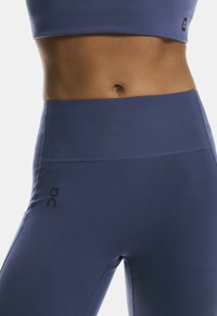 Nærbillede af en persons mave iført højttaljede navy blå træningstights og en matchende sports-bh.