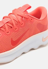 Koral Nike sneakers med teksturert mesh-overdel, snøring og en polstret hvit mellomsåle med ferskenfargede detaljer.