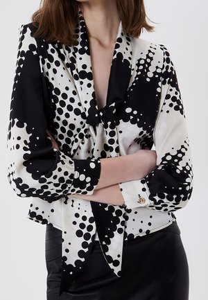 Schwarz-weiße Bluse mit Polka-Dot-Muster, Wickel-Front-Design und langen Ärmeln mit geknöpften Manschetten. Glatter Stoff mit einer Schleifendetail.