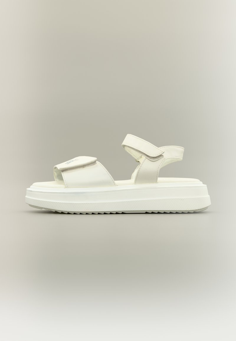 Sandale plateforme blanche avec des brides ajustables et une semelle épaisse texturée, vue de profil sur un fond neutre.