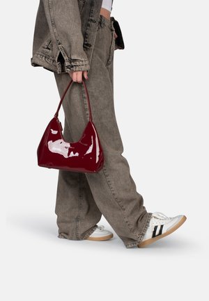Burgundy patent handbag with a curved, triangular shape and a single handle, paired with gray baggy jeans and white sneakers.