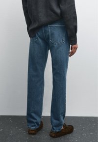 Blå denimjeans med lös passform, med bakfickor och subtila blekningar. Tillsammans med en mörk knäppskjorta och bruna skor.