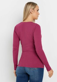 Langärmliges Oberteil in tiefem Magenta, mit figurbetonter Silhouette und weichem, dehnbarem Stoff; Rundhalsausschnitt und glatte Textur.