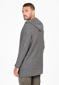 Giacca con cappuccio grigio in lana, dal taglio lungo, caratterizzata da una finitura testurizzata e una vestibilità comoda. Include una tasca a marsupio e polsini a coste.