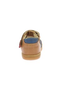 Chaussure en cuir pour enfant avec un corps couleur tan, des côtés bleus et un bouton décoratif rouge. Elle dispose d'une sangle en Velcro et d'une semelle en caoutchouc texturé.