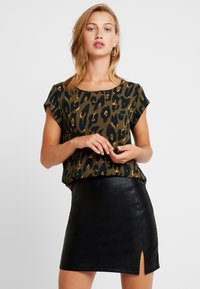 Top a maniche corte, verde oliva con stampa leopardata nera, abbinato a una mini gonna in pelle nera con spacco laterale.